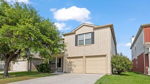 A two-story residential building with a beige brick exterior, a front garage, and a well-maintained lawn.
