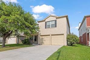 A two-story residential building with a beige brick exterior, a front garage, and a well-maintained lawn.