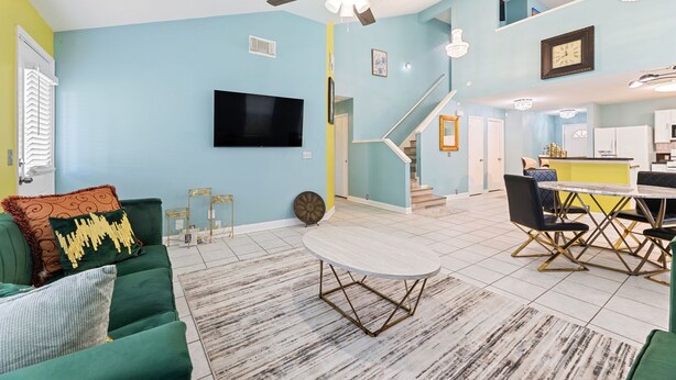 Een ruime woonkamer met een groene bank, een ronde salontafel en een trap naar een keukenhoek.