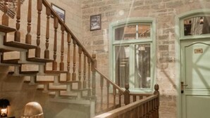 Una escalera con balaustres de madera que conduce a una barandilla de vidrio, una pared de piedra, una puerta verde y un candelabro colgante.