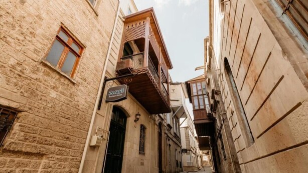 Una estrecha calle adoquinada bordeada por edificios históricos con balcones y un letrero que indica 'Sazeli Boutique Hotel'.