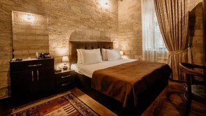 Un dormitorio con pared de piedra, cabecera de madera, cama con ropa blanca, mesita de noche con lámpara y una silla.