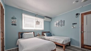A bedroom with two beds, a window with blinds, a hanging light fixture, and a door with a window. - Seashore Condo Hotel #5, Cozy Fire Island Escape, Near Ferry - With Bay Views and Steps from the Beach. (Ocean Bay Park)