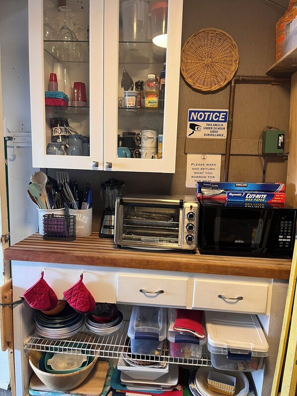 A kitchen with a microwave, toaster, and various kitchen utensils. There is a notice sign on the wall and a basket on the counter.
