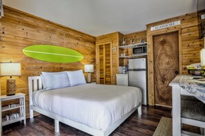 Un dormitorio con cama, mesitas de noche, microondas, refrigerador y una pared de madera con un cartel que dice 'SEASHORE'.