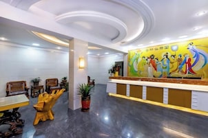 A hotel reception area with a modern design, featuring a reception desk, seating area, and a mural on the wall.