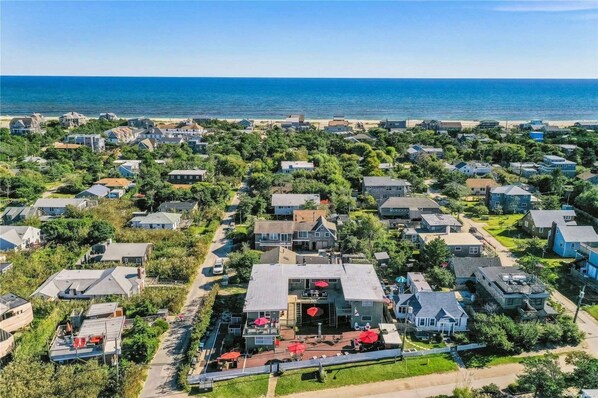 Zona residencial a la costa amb cases, un edifici central amb un paraigua vermell i una platja al fons.