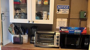 A kitchen with a microwave, toaster, and various kitchen utensils. There is a notice sign on the wall and a basket on the counter.