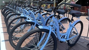 A row of blue bicycles parked on a wooden deck with red umbrellas overhead.