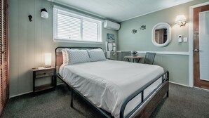 A bedroom with a bed, bedside table, lamp, and a small table with a chair.