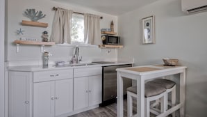 A modern kitchen with white cabinetry, a stainless steel dishwasher, and a small dining table with two chairs.