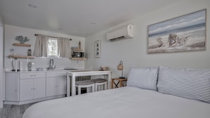 A bedroom with a large bed, a small desk, a chair, a nightstand, and a painting of a beach scene.