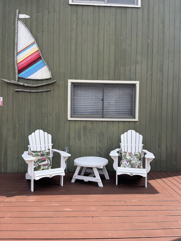 A wooden deck with two white Adirondack chairs and a small round table.