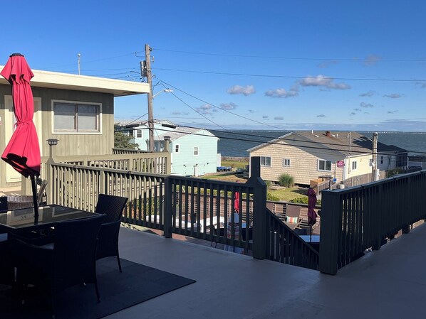 A balcony with a table and chairs, overlooking a residential area and the ocean.