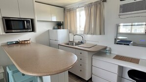 A compact kitchen with a microwave, refrigerator, sink, and a small dining area with stools.