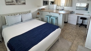 A bedroom with a bed, a desk, a chair, a microwave, a refrigerator, and a window with curtains.