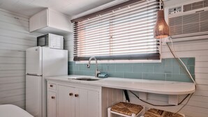 Een kleine keuken met een witte koelkast, een spoelbak en een raam met zonwering.