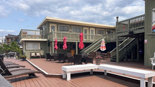 A wooden deck with outdoor seating, a staircase, and a building with numbered windows.