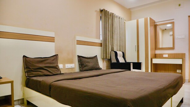 A hotel room with a large bed, a bedside table, a wardrobe, and a mirror. - Virksham Hotel (Coimbatore)