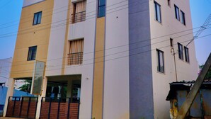A multi-story building with a flat roof, several balconies, and a visible entrance with a gate. - Virksham Hotel (Coimbatore)