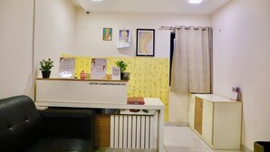 A reception area with a desk, a black leather chair, a potted plant, and a calendar on the wall. - Virksham Hotel (Coimbatore)