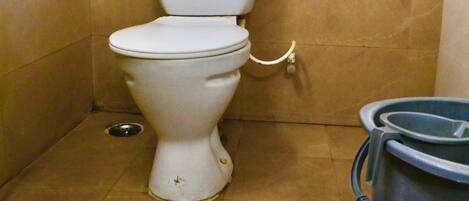 Ein kleines Badezimmer mit Toilette, einem Metallablauf und einem blauen Eimer.