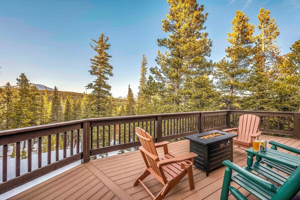 A wooden deck with outdoor seating, a fire pit, and a view of a forest.