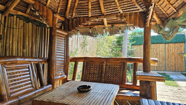 Een houten terras met een tafel en banken, omgeven door bamboe wanden en een rieten dak.