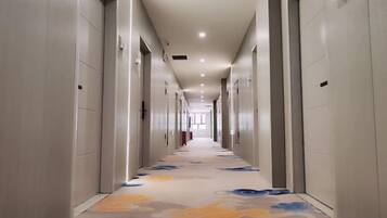A long, narrow hotel corridor with doors on both sides, a patterned carpet, and recessed lighting.