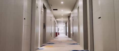 A long, narrow hotel corridor with doors on both sides, a patterned carpet, and recessed lighting.