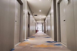 A long, narrow hotel corridor with doors on both sides, a patterned carpet, and recessed lighting.