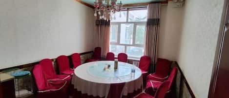 A dining room with a round table, red upholstered chairs, a chandelier, and a window with curtains.