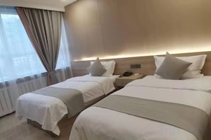 A hotel room with two beds, a bedside table with a lamp, and a window with curtains.