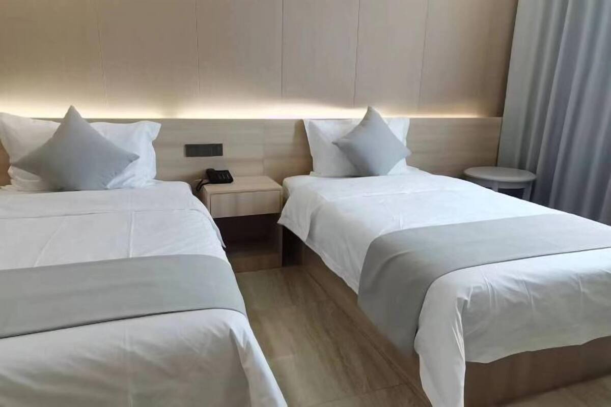 A hotel room with two beds, a bedside table with a phone, and a small stool.