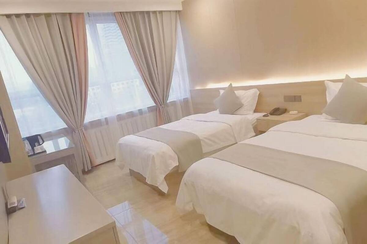 A hotel room with two beds, a desk, and a view of the city.