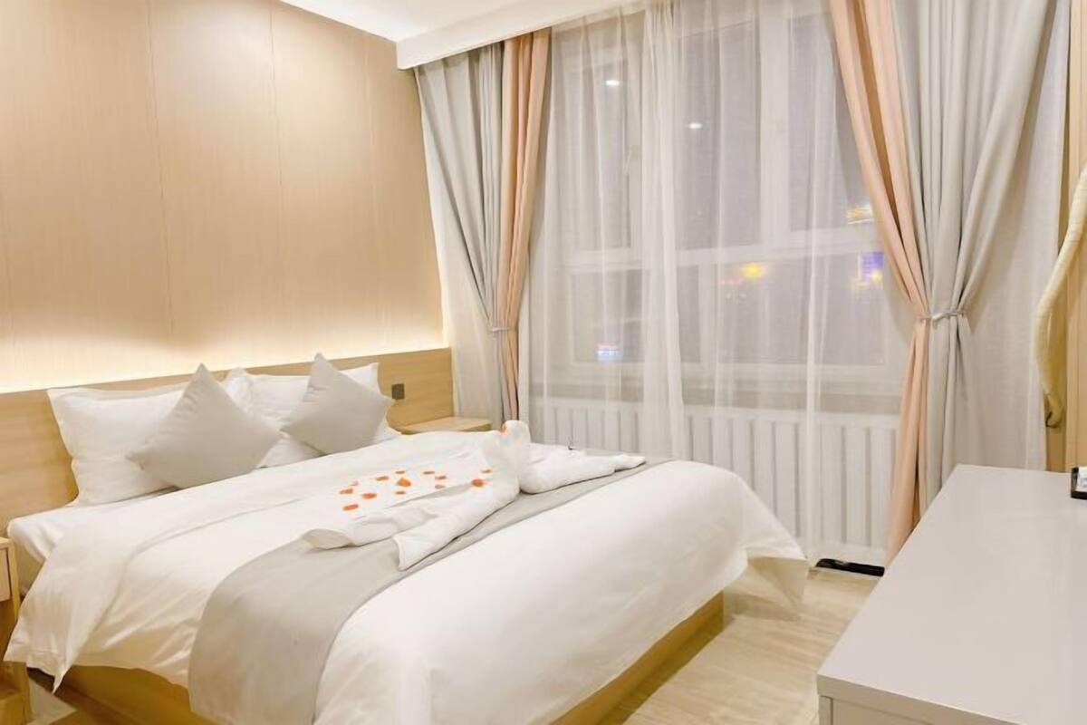 A hotel room with a bed, a bedside table, and a window with sheer curtains.