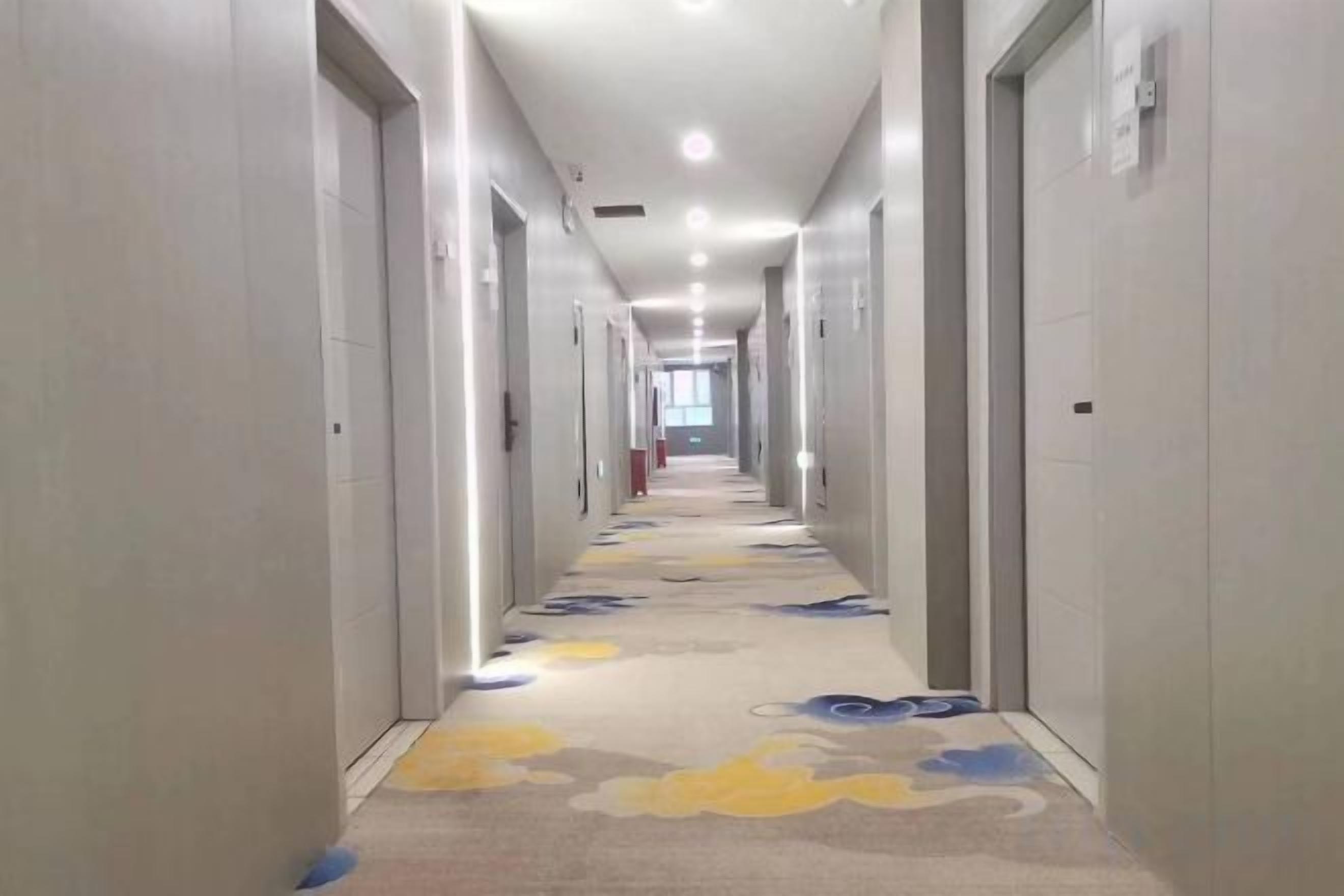 Ein Hotelgang mit Türen auf beiden Seiten, mit einem floralen Teppichboden und einer Decke mit eingelassenen Leuchten.
