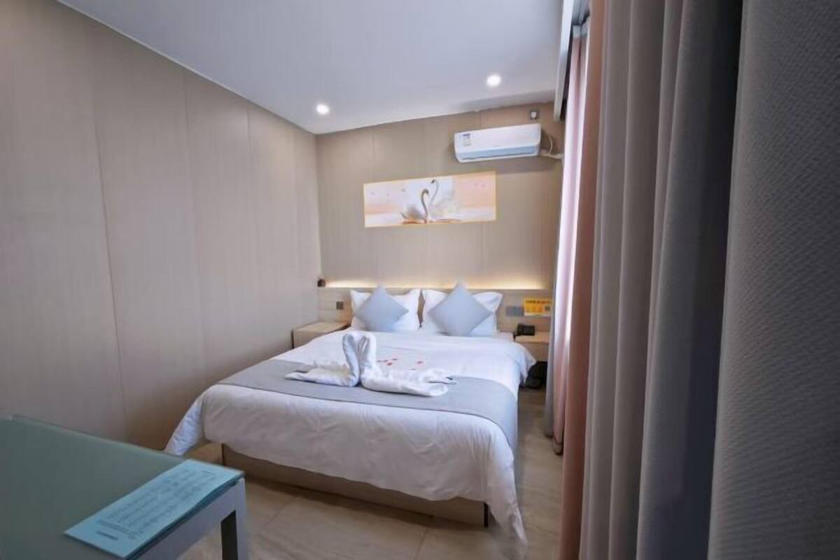 A hotel room with a bed, a nightstand, an air conditioning unit, and a wall-mounted artwork.