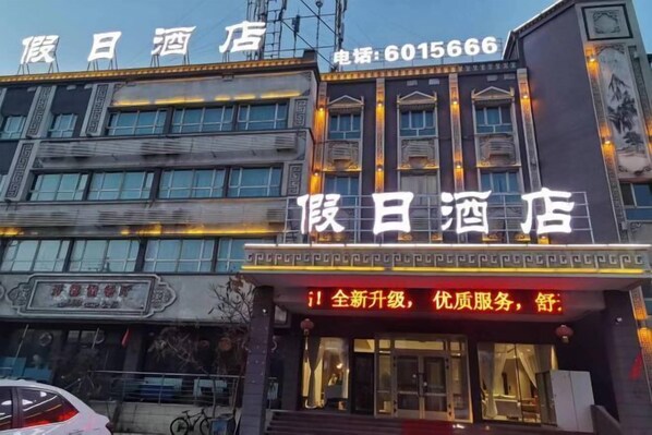 A hotel facade with illuminated signage, a contact number, and a traditional architectural style.