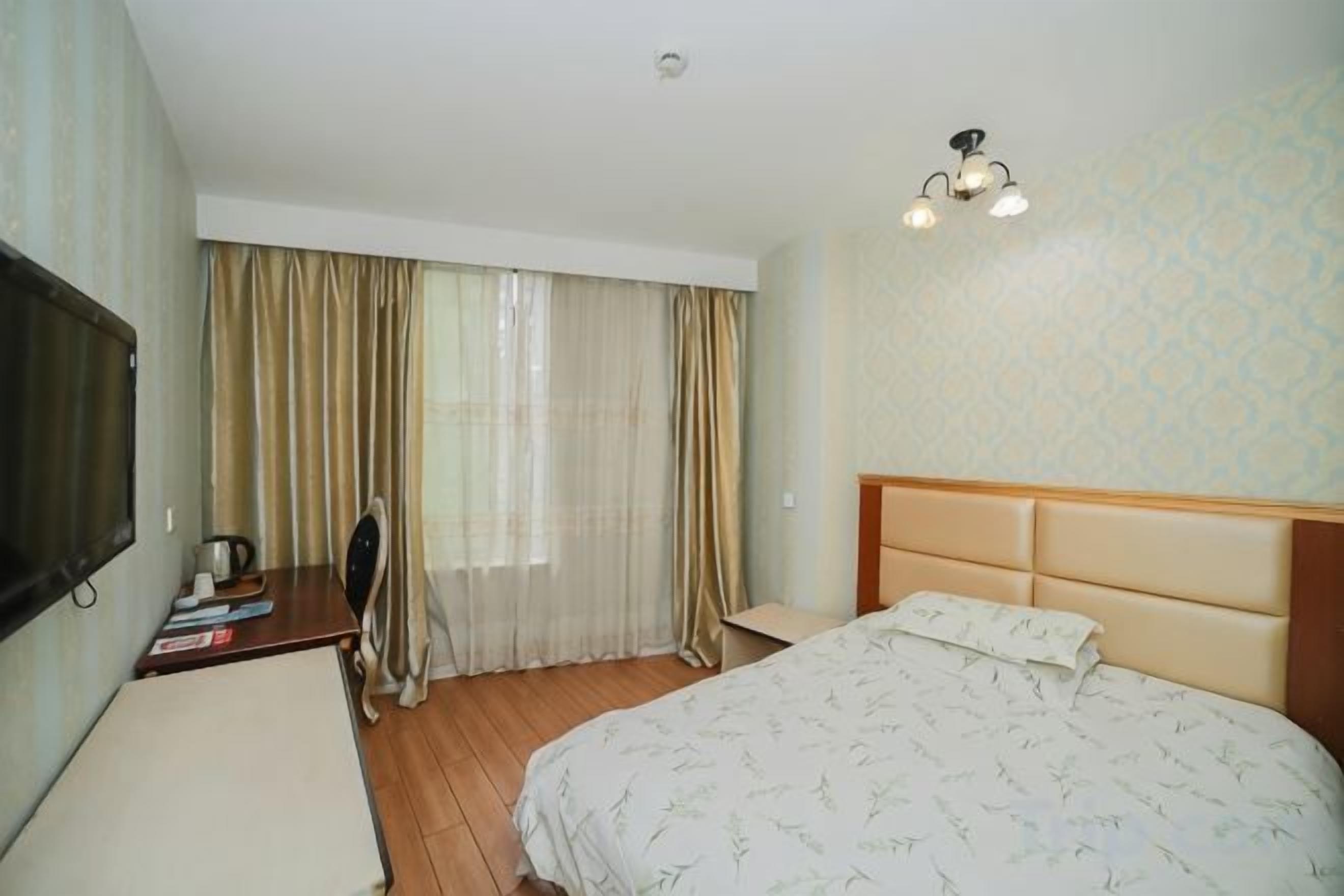 A hotel room with a bed, a desk with a chair, a television, and a window with curtains.