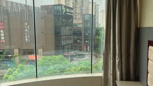 A hotel room with a large window offering a view of a cityscape, including modern buildings and a street. - Huchen Fashion Hotel (Shanghai)