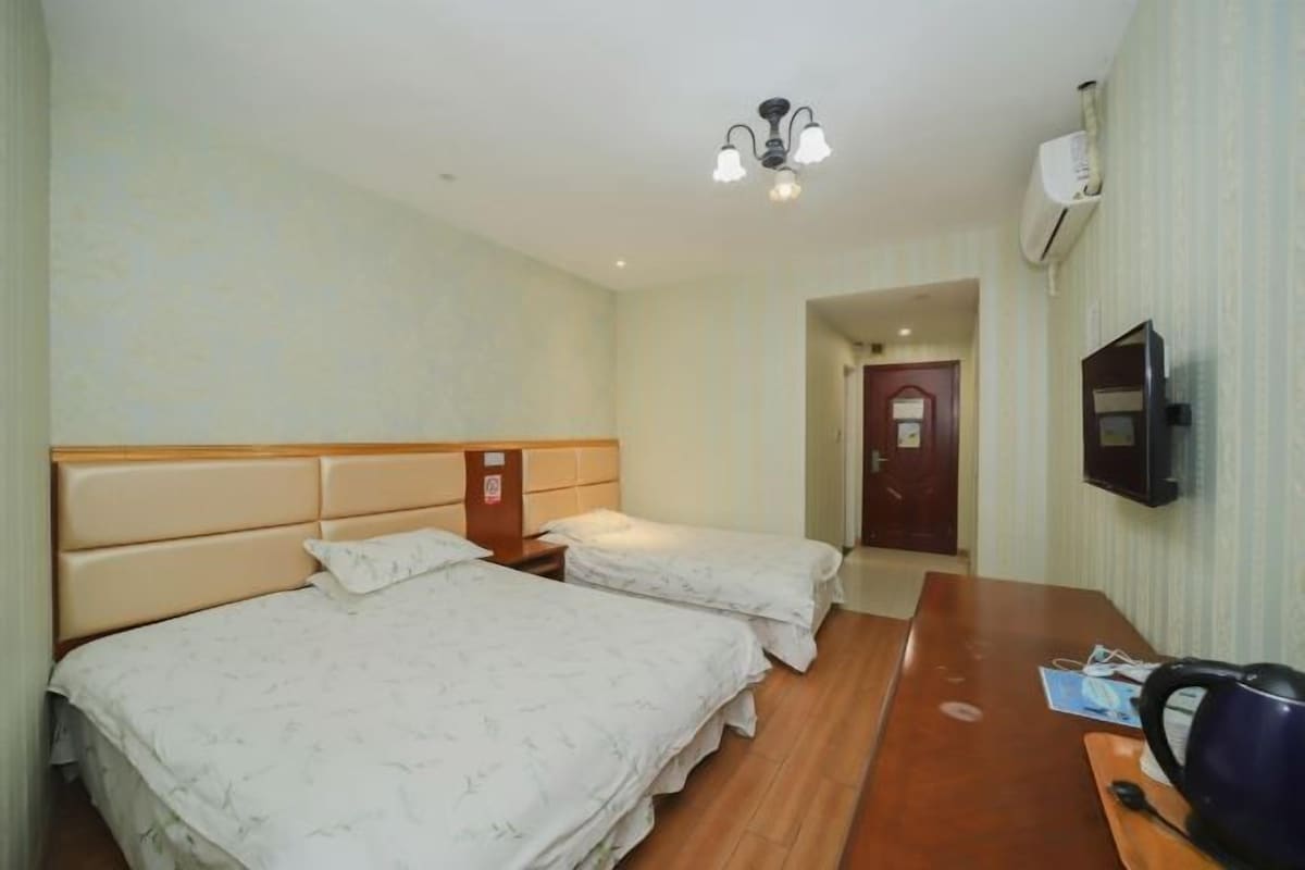 A hotel room with two beds, a wooden desk, a kettle, and a television.