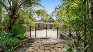 A tropical garden with a stone pathway leading to a house with a pool.