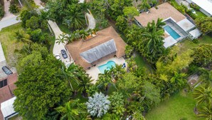 An aerial view of a residential property with a swimming pool, a detached garage, and lush greenery.