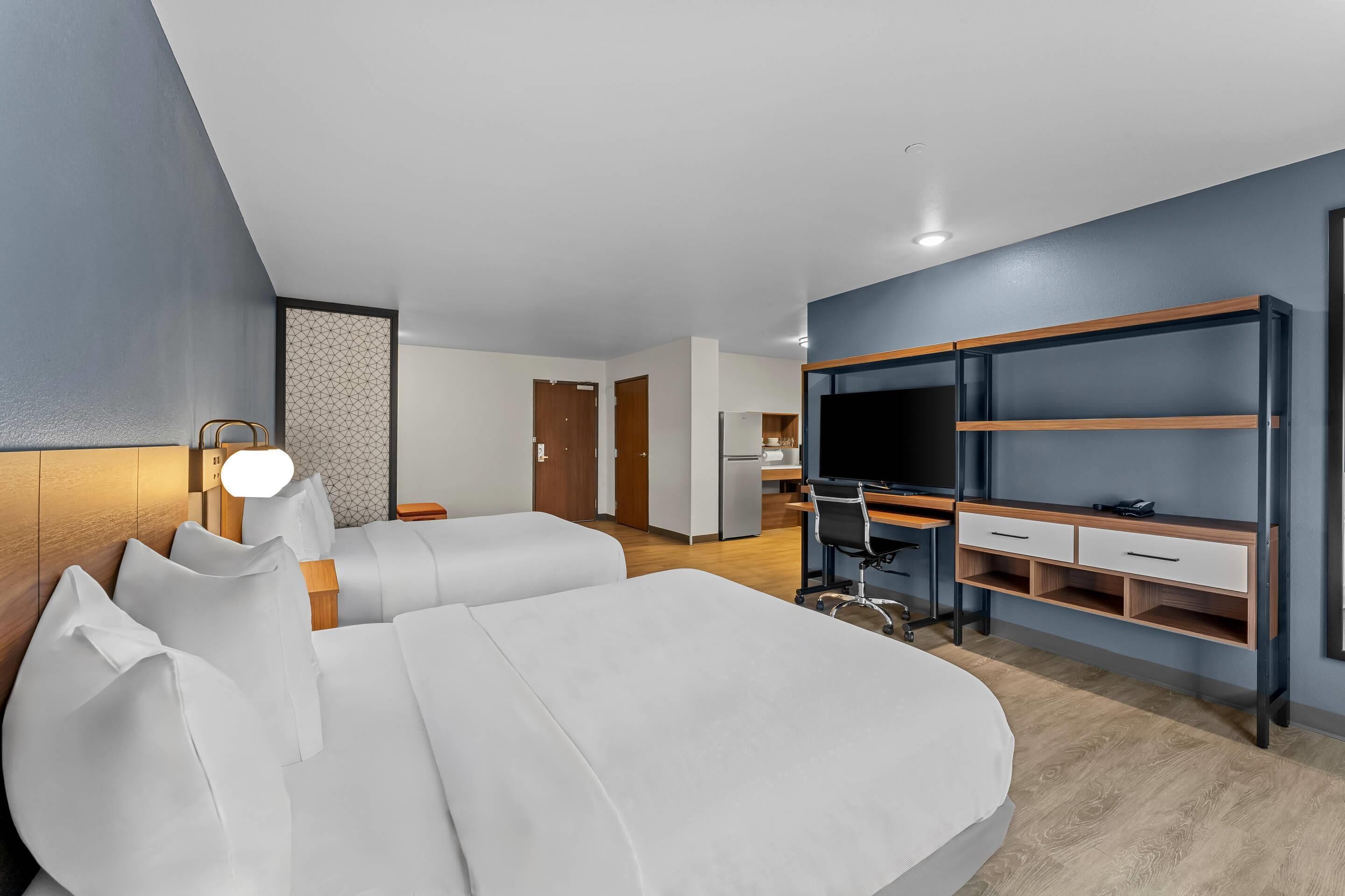 A modern hotel room with a large bed, a desk with a chair, a TV, and a wardrobe.