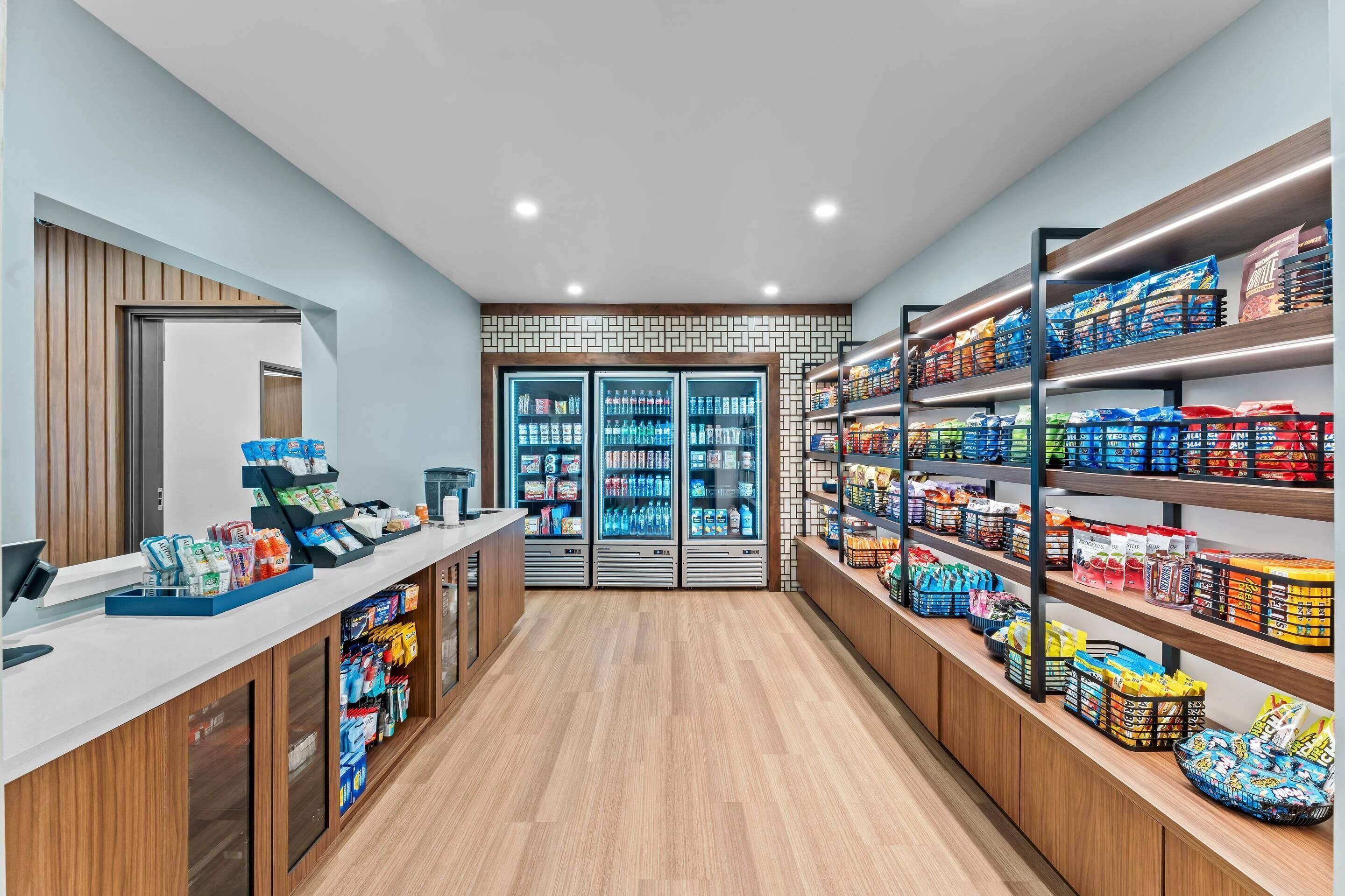 Un espacio comercial moderno con una caja registradora, vitrinas refrigeradas y estantes llenos de aperitivos y bebidas.