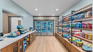 Un espacio comercial moderno con una caja registradora, vitrinas refrigeradas y estantes llenos de aperitivos y bebidas.