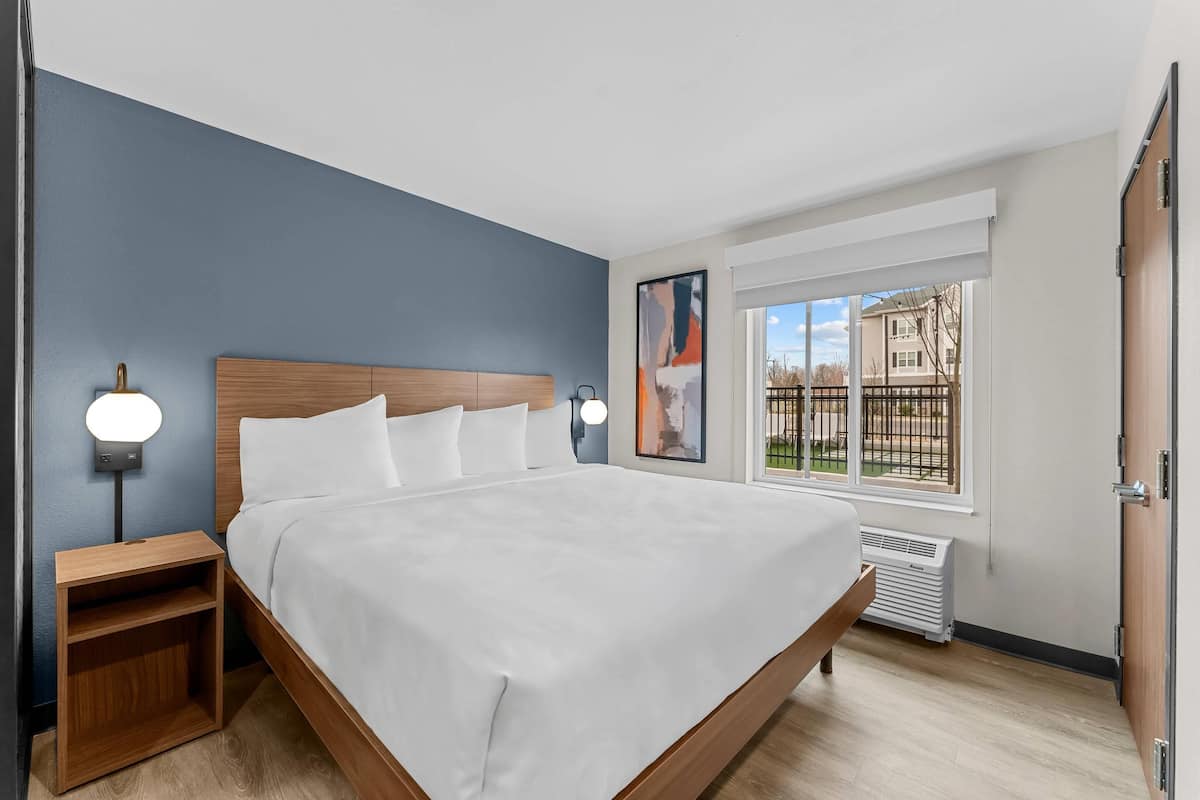 A bedroom with a bed, nightstands, a window with a view, and a door.