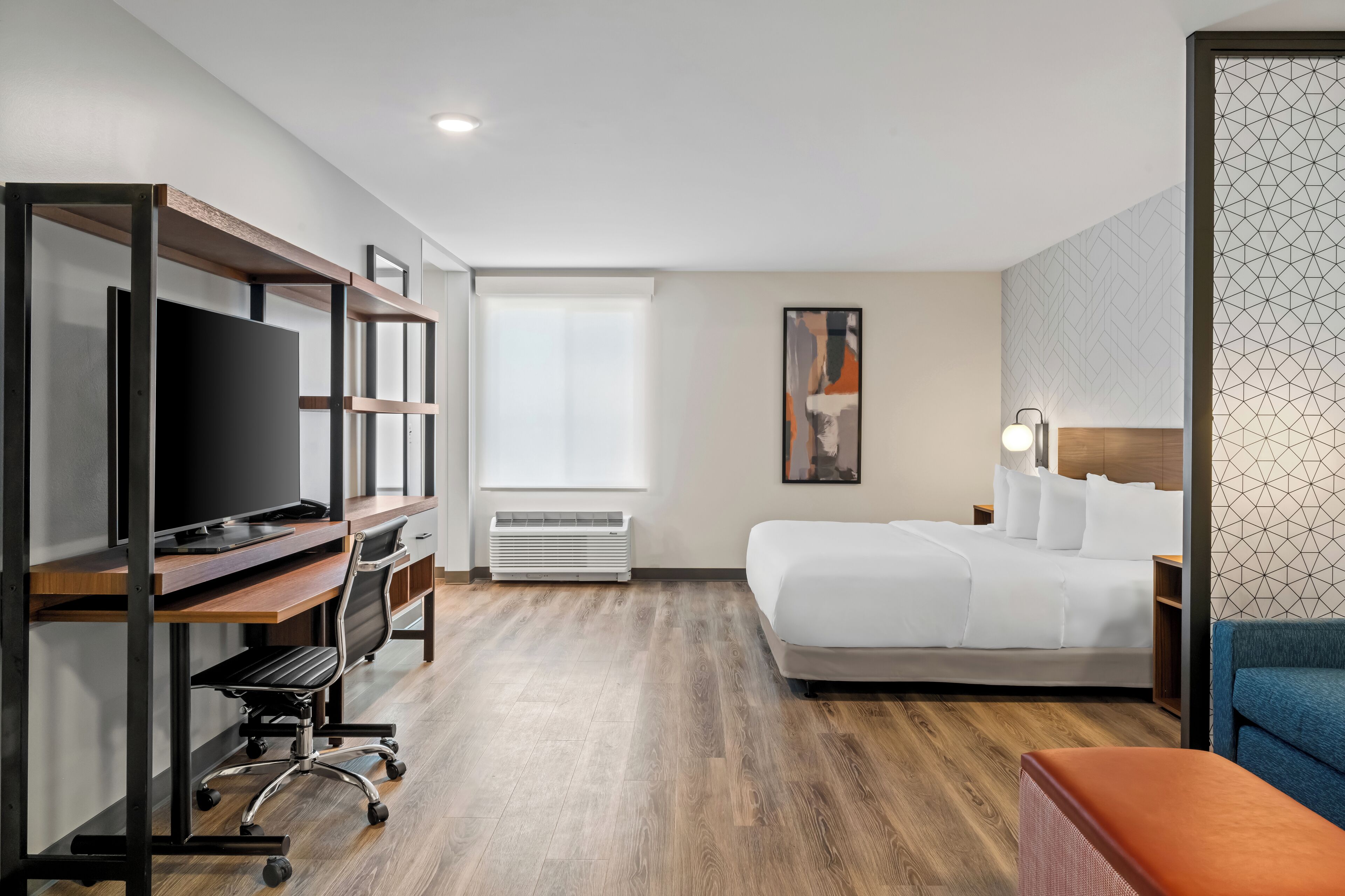 A hotel room with a bed, a desk with a TV, a chair, a heater, and a window.