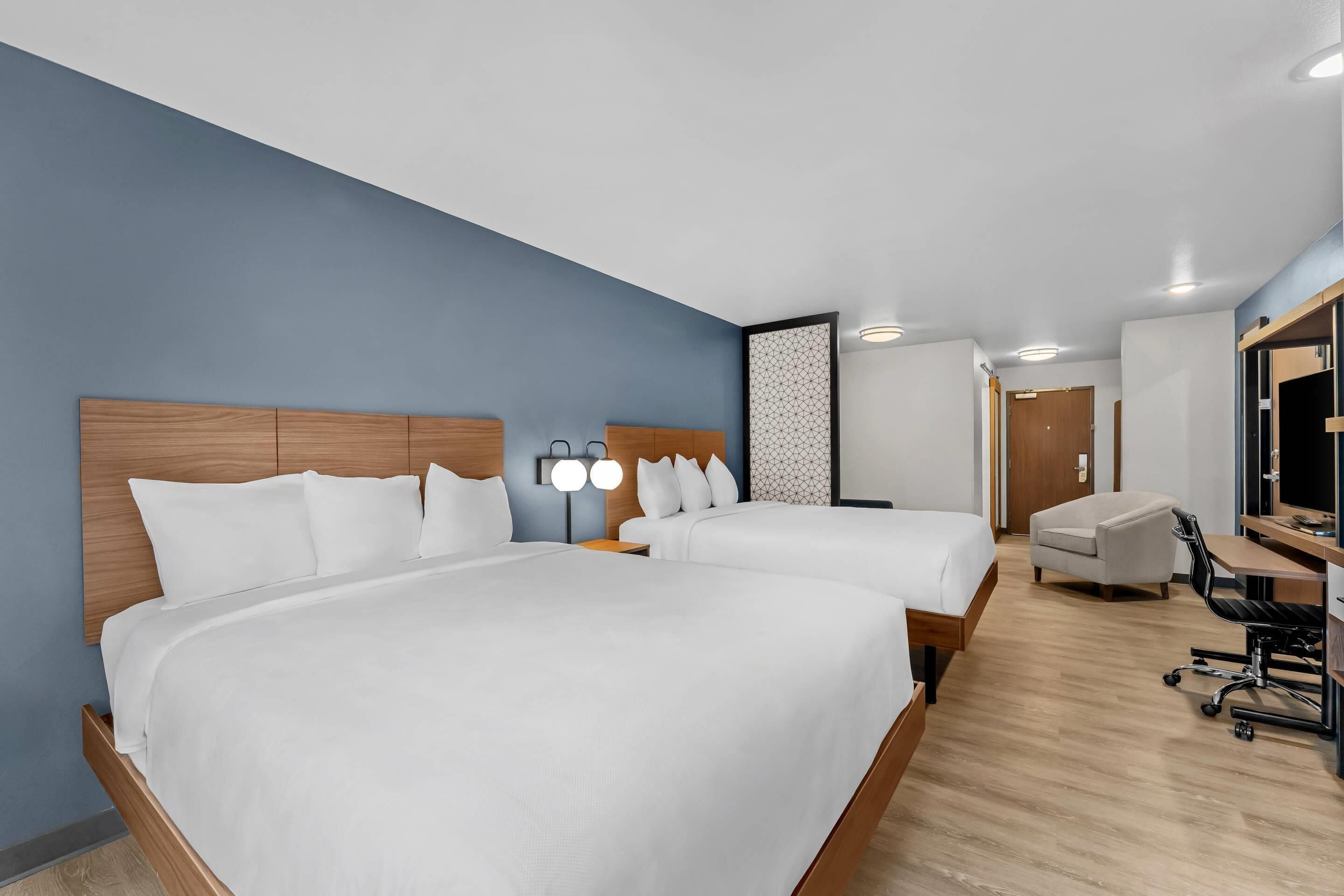 Ein Hotelzimmer mit zwei Betten, einem Schreibtisch, einem Stuhl und einem großen Spiegel.
